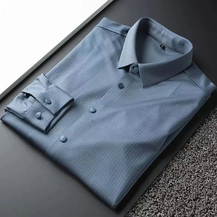 A neatly folded light blue men's slim shirt with matching buttons rests on a dark surface next to a section of gray carpet, perfect for business casual or spring long-sleeved shirt styles.
