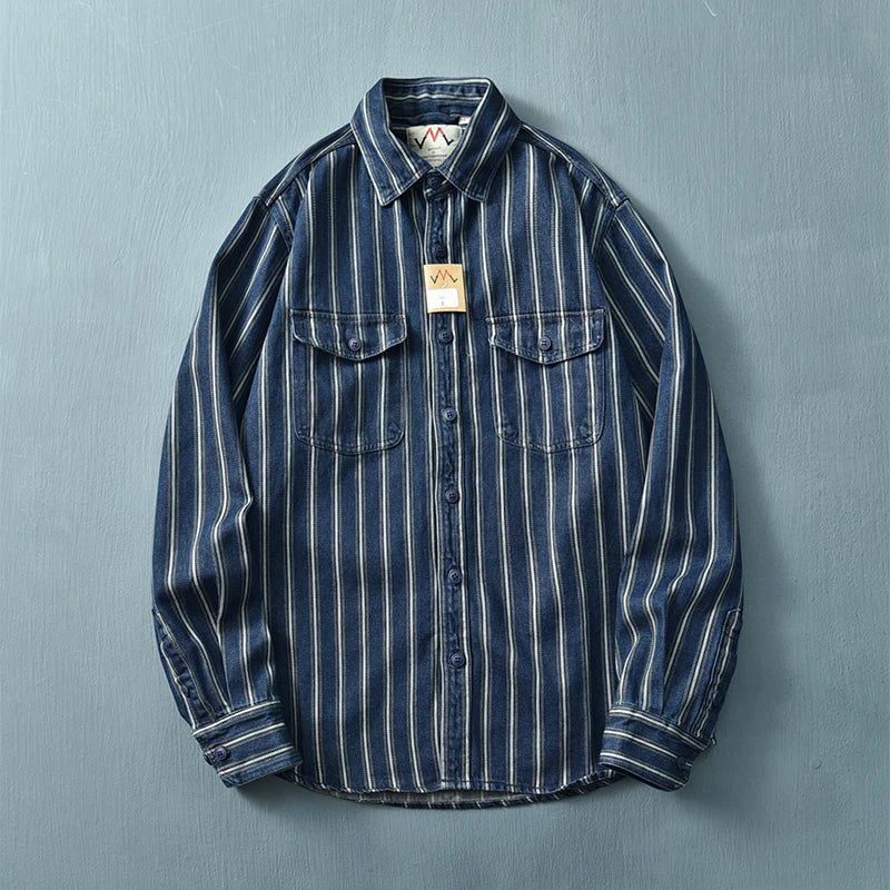 A relaxed fit, long-sleeve denim shirt crafted from heavyweight cotton with vertical white and blue stripes, vintage button-up front, and two chest pockets with flaps, displayed flat against a light blue background.