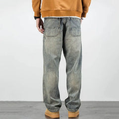 A person wearing classic fit, faded baggy jeans with two large rear pockets, a brown sweatshirt, and tan shoes stands facing away, showcasing the straight leg jeans from behind.