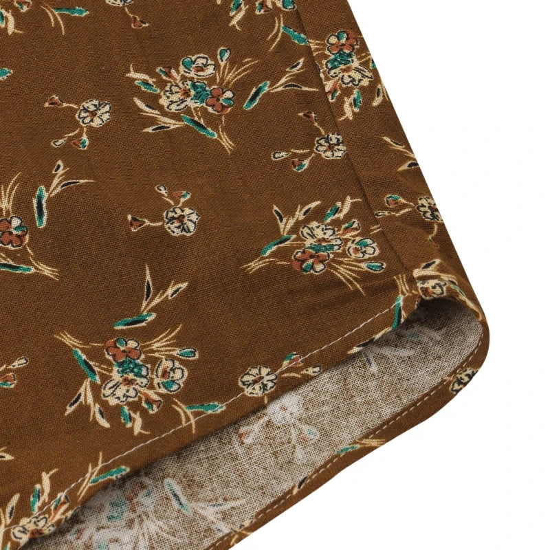 Close-up of brown fabric with a floral pattern in green, cream, and rust tones. The edge is folded, revealing the lighter underside with a faint outline—perfect for a classic design on a casual cotton shirt.