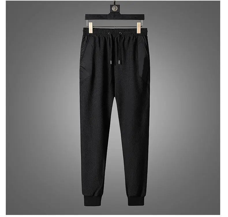 Black jogger pants with an elastic waistband, drawstring, and cuffed ankles, part of an activewear set, displayed hanging on a wooden hanger against a plain gray background.