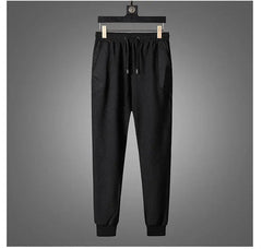 Black jogger pants with an elastic waistband, drawstring, and cuffed ankles, part of an activewear set, displayed hanging on a wooden hanger against a plain gray background.