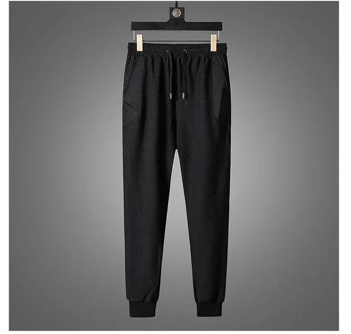 Black jogger pants with an elastic waistband, drawstring, and cuffed ankles, part of an activewear set, displayed hanging on a wooden hanger against a plain gray background.