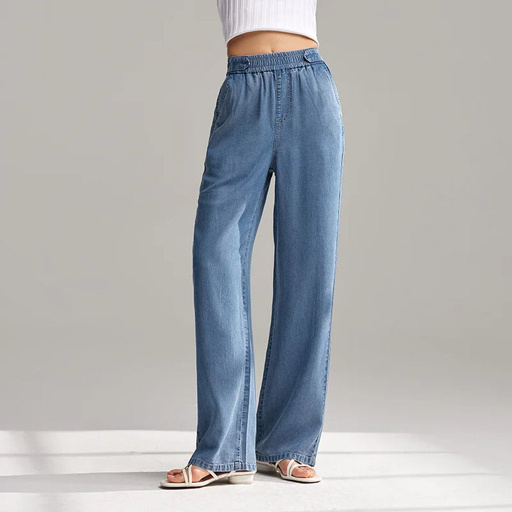 A person wearing wide-leg, light blue breathable denim pants with an elastic waistband and white sandals stands against a plain background. Only the lower torso and legs are visible.