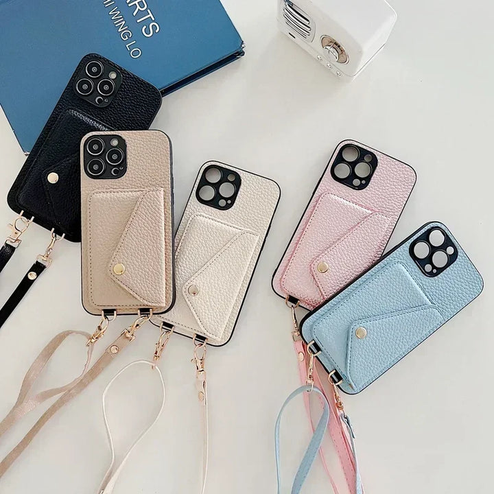 Five smartphones with pebble-texture material wallet-style cases in black, beige, pink, and blue are arranged on a white surface. Each case features a wrist strap and a cardholder pocket. A blue notebook and a small white device are also visible.