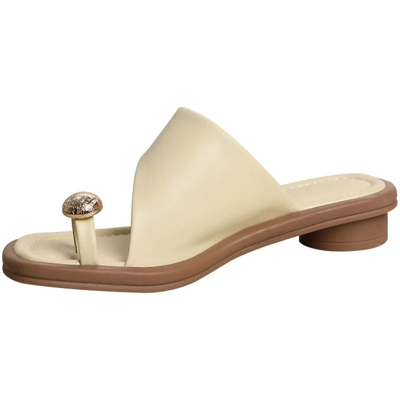 A beige open-toe sandal with a low brown heel, featuring a wide strap and a unique round, jeweled toe separator on the footbed—perfect for those who love fashionable slides.