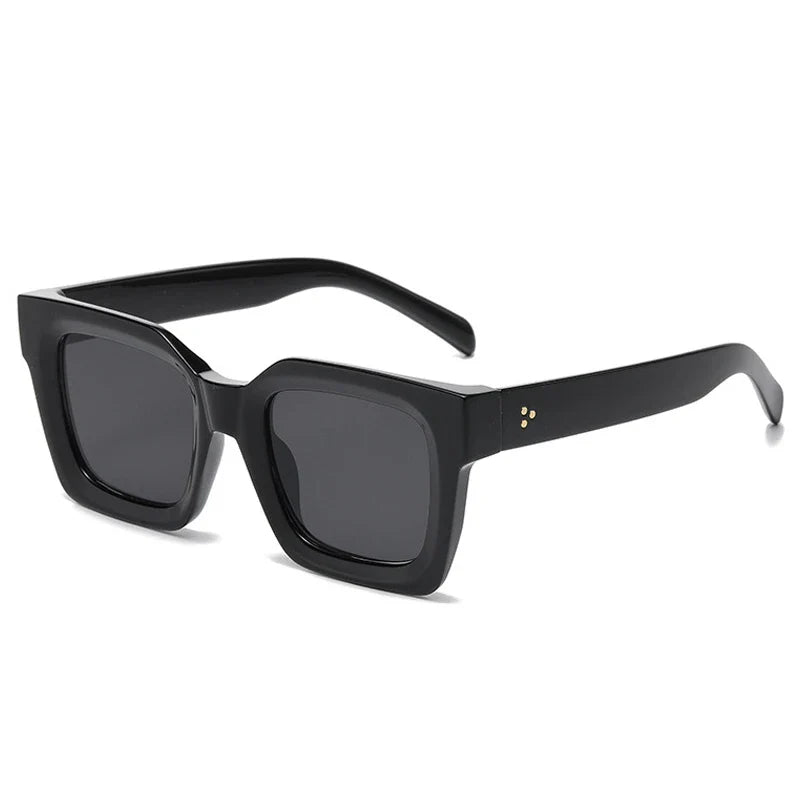 Black square-framed sunglasses with dark lenses and thick acetate frames, featuring small gold dots on the hinge area, displayed on a white background. These sunglasses offer both style and UV protection.