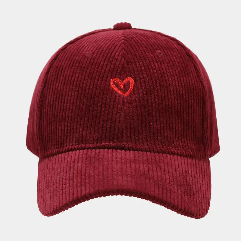 A burgundy corduroy baseball cap with a FlexFit band and a small red heart embroidered on the front, displayed against a plain white background.