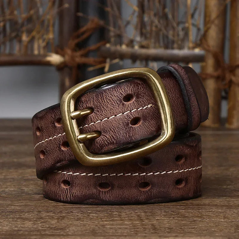 A genuine leather belt showcasing heritage craftsmanship, with white stitching and a large brass buckle, is coiled on a wooden surface against a rustic background.