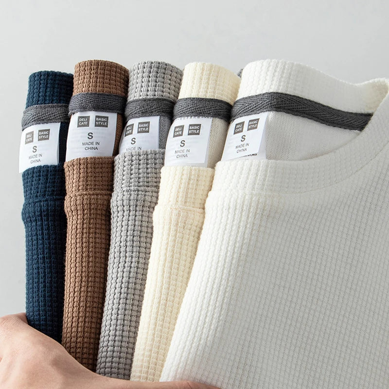A hand holds five folded ribbed shirts in navy blue, brown, gray, light beige, and white. Each heavyweight shirt is crafted from 260G cotton with a visible clothing tag showing the size S and care information.