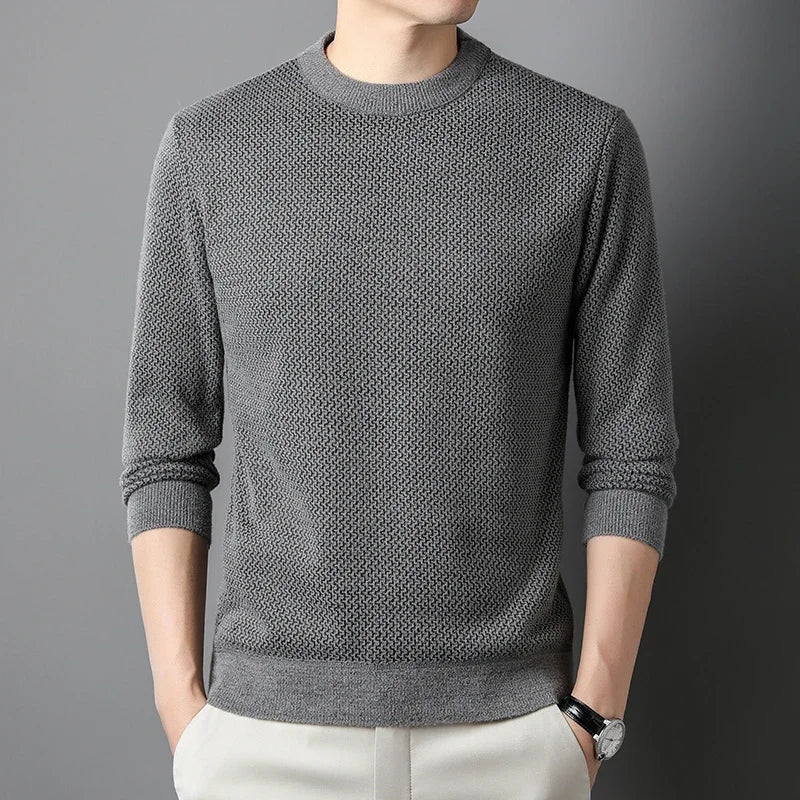 A person wearing a versatile gray knit sweater with long sleeves, light-colored pants, and a wristwatch, standing against a plain gray background. The persons head is not visible.