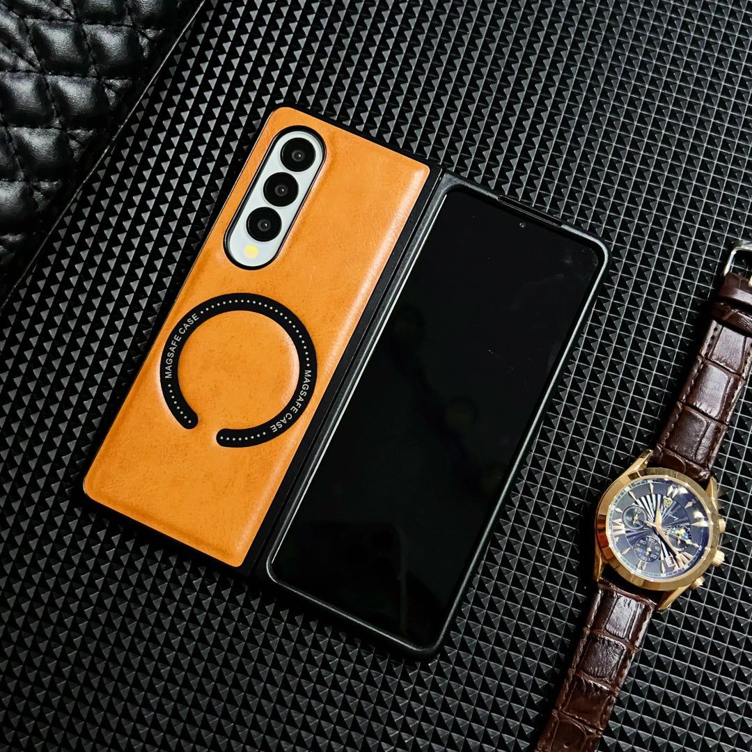 A foldable smartphone with a tan Samsung Galaxy Z Fold case lies partially open on a textured black surface, next to a brown leather strap watch and a quilted black item.