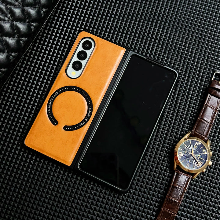 A foldable smartphone with a tan Samsung Galaxy Z Fold case lies partially open on a textured black surface, next to a brown leather strap watch and a quilted black item.