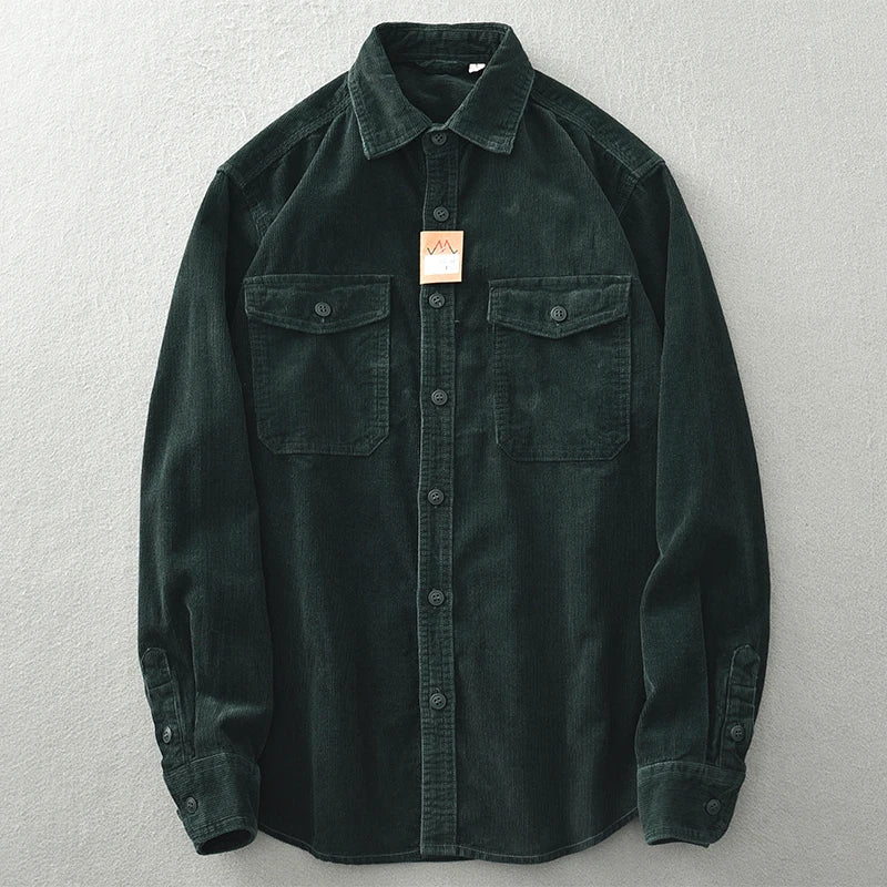 A dark green button-up shirt with corduroy detailing, long sleeves, two front chest pockets with flaps, and a small beige tag near the collar, laid flat on a light gray surface.