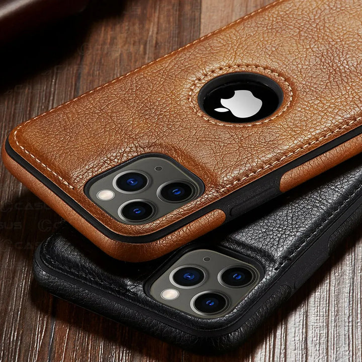 Two smartphones in brown and black luxury leather phone cases rest on a wooden surface. Both slim protective cases feature a circular cutout revealing the Apple logo, openings for the triple camera, and are wireless charging compatible.