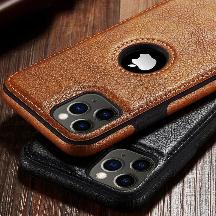 Two smartphones with luxury leather phone cases, one in brown and one in black, rest on a wooden surface. The brown slim protective case has a circular cutout revealing the Apple logo and is wireless charging compatible.