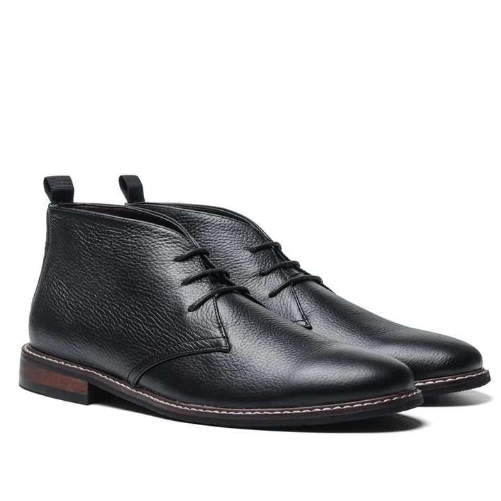 A pair of black After-Ride Chukka leather boots with laces, a textured finish, and brown rubber soles with a small heel. These Western-inspired chukka boots feature pull tabs at the back and visible white stitching around the soles.