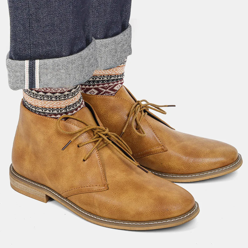 A person wearing cuffed dark jeans, patterned socks, and Western-inspired chukka boots crafted from premium leather stands on a light background.