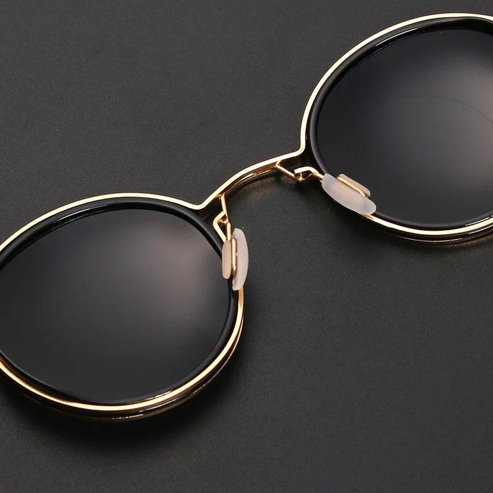 Gold-framed round Ruby Ray Sunglasses with black lenses placed on a dark surface, showing the bridge and nose pads in clear detail; offers UV400 protection for optimal eye safety.