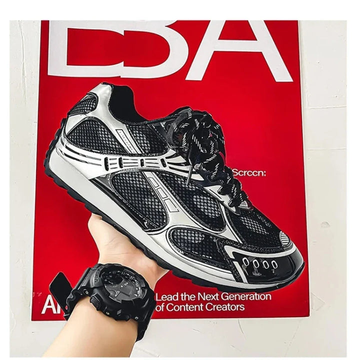 A hand wearing a black watch holds up a black and silver athletic sneaker with a cushioned insole in front of a red poster with white text on a white wall.