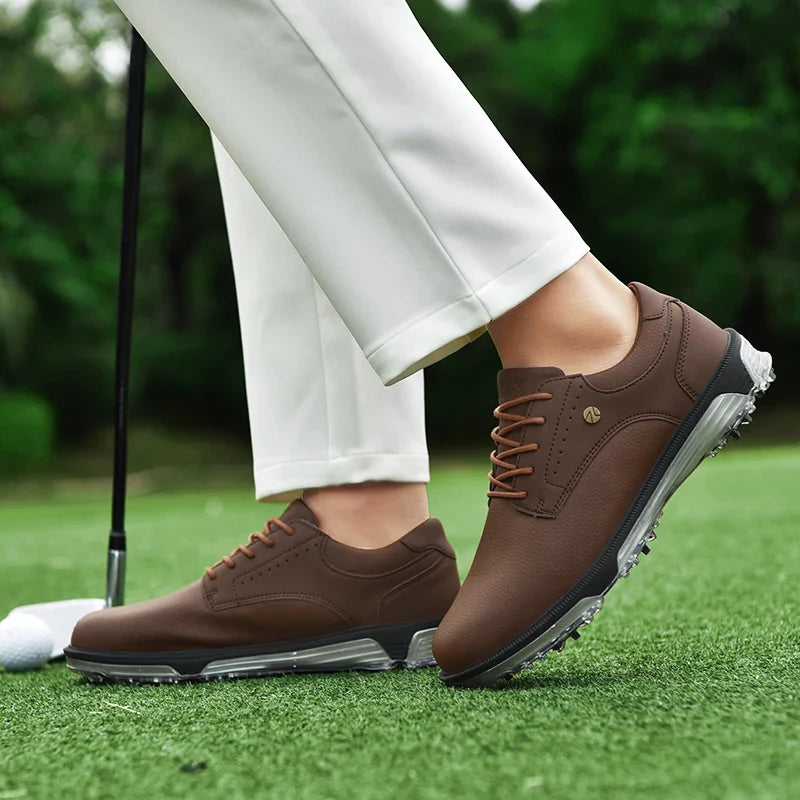 A person wearing white pants and brown genuine leather golf shoes stands on green grass next to a golf ball and club, with a blurred green background.