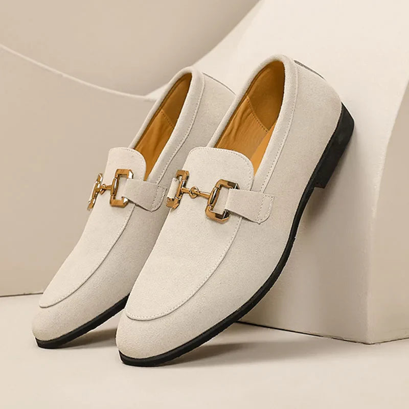 A pair of elegant beige suede luxury loafers with gold horsebit detailing on the front, black soles, and a cushioned insole for added comfort, displayed against a neutral background.