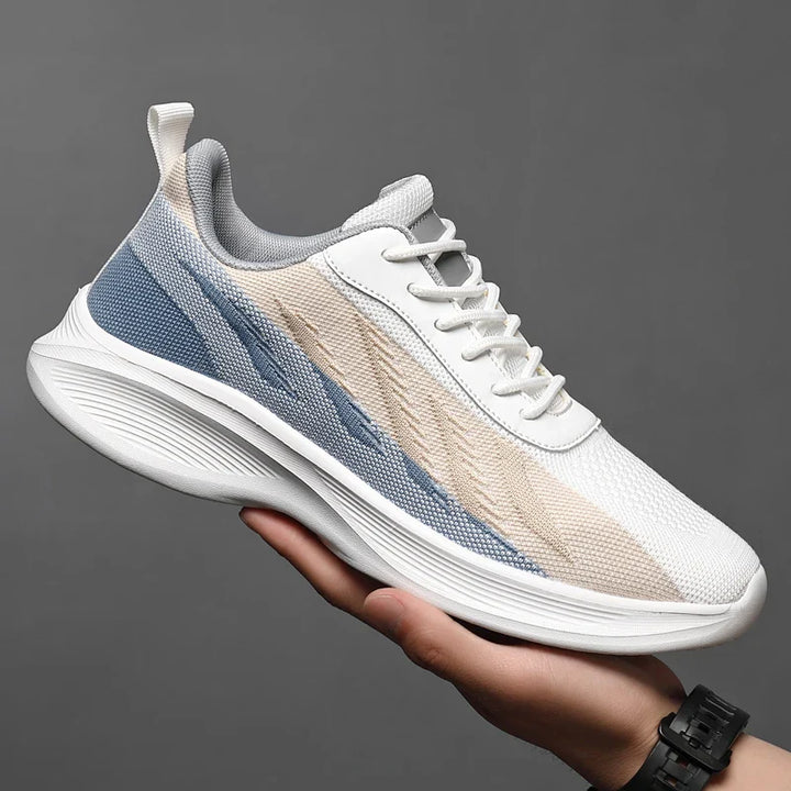 A person holds a modern athletic sneaker with a white sole, white laces, and a gradient upper in shades of white, beige, and blue—perfect workout shoes featuring breathable mesh for comfort against a plain gray background.
