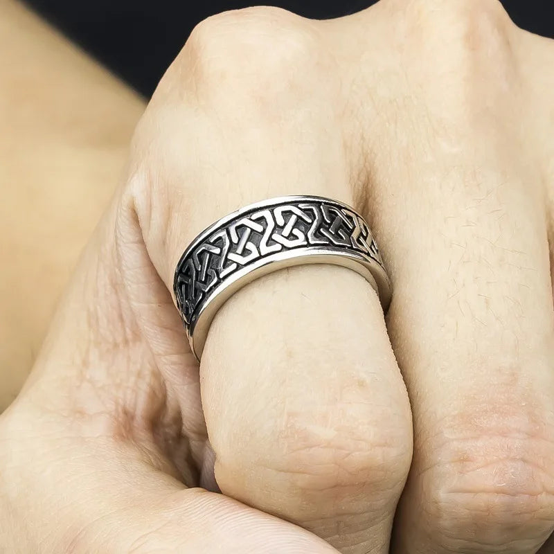 A close-up of a hand wearing a Celtic knot ring, featuring an intricate pattern engraved around the band on a durable metal ring.