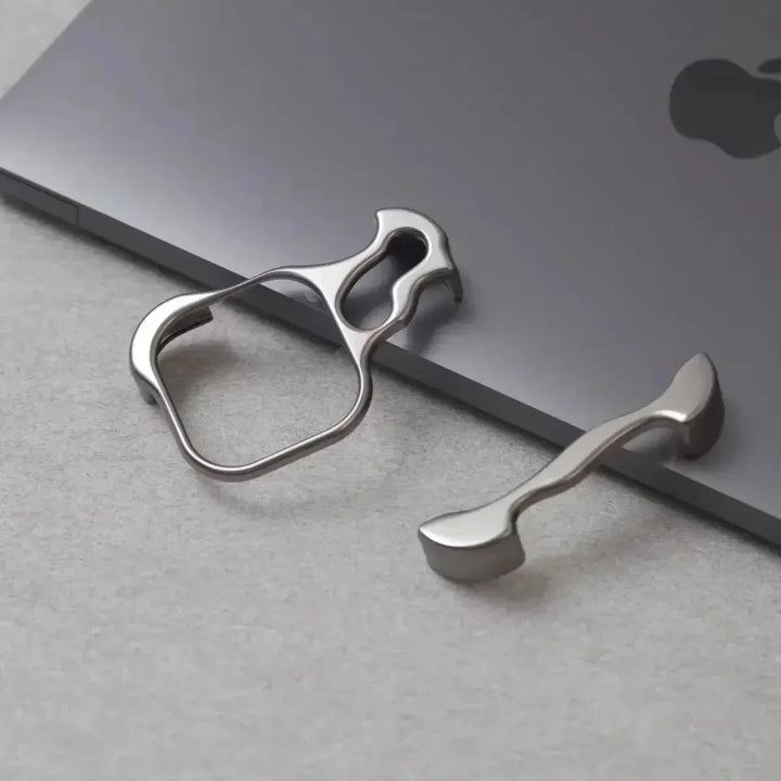 Two metallic bottle openers with a sleek metal bumper design rest on a closed, gray laptop with an Apple logo, all placed on a light gray surface.