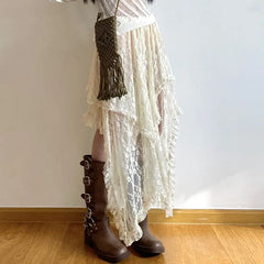 Person wearing a white, high waist asymmetrical lace skirt with a silky lace finish, brown knee-high boots with multiple buckles, and an olive green woven crossbody bag, standing on a wooden floor against a plain white wall.