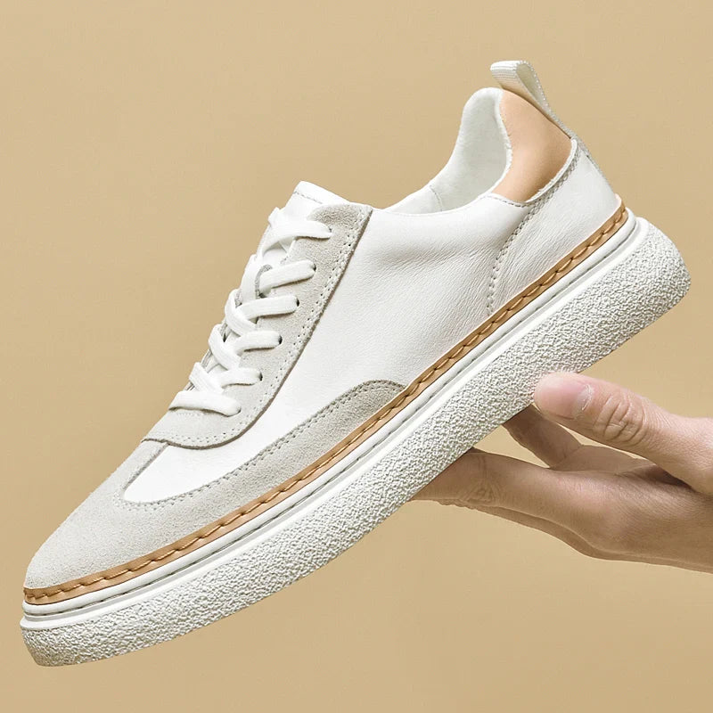 A hand holds up a white sneaker with light beige accents, a textured white sole, and tan stitching details against a plain beige background, highlighting its cushioned insole for extra comfort.