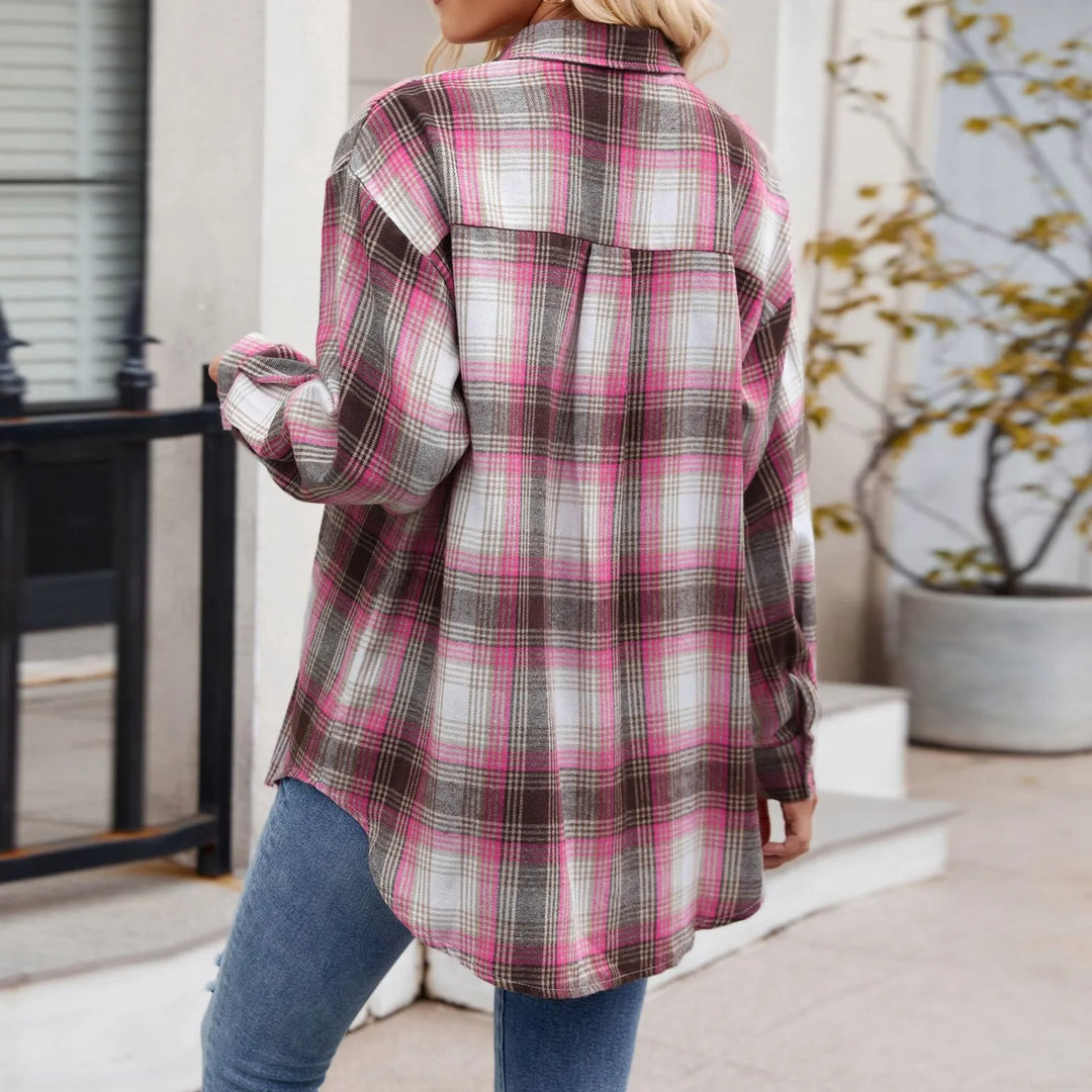 A person wearing an oversized fit, long-sleeved plaid button-down shirt in shades of pink, grey, and white with blue jeans is standing outdoors with their back to the camera.
