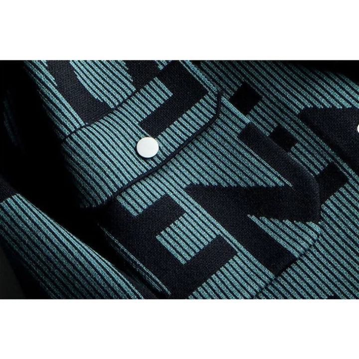 Close-up of a vintage knitted cardigan with a blue and black striped pattern, featuring large, bold black letters and two white buttons on a flap or pocket.