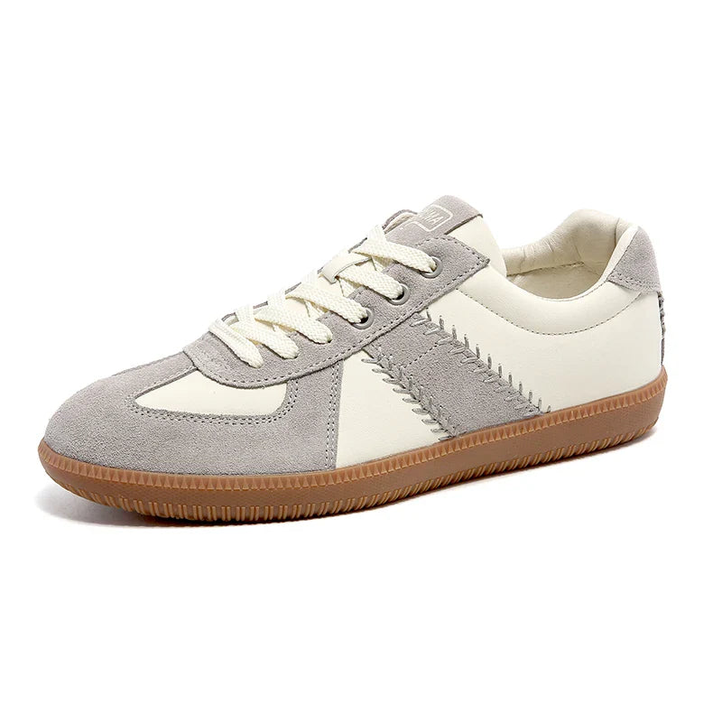 A stylish sneaker with a gray suede toe and trim, off-white leather panels, white laces, decorative stitching, and a textured brown rubber sole—these lightweight breathable sneakers offer comfort and modern appeal.