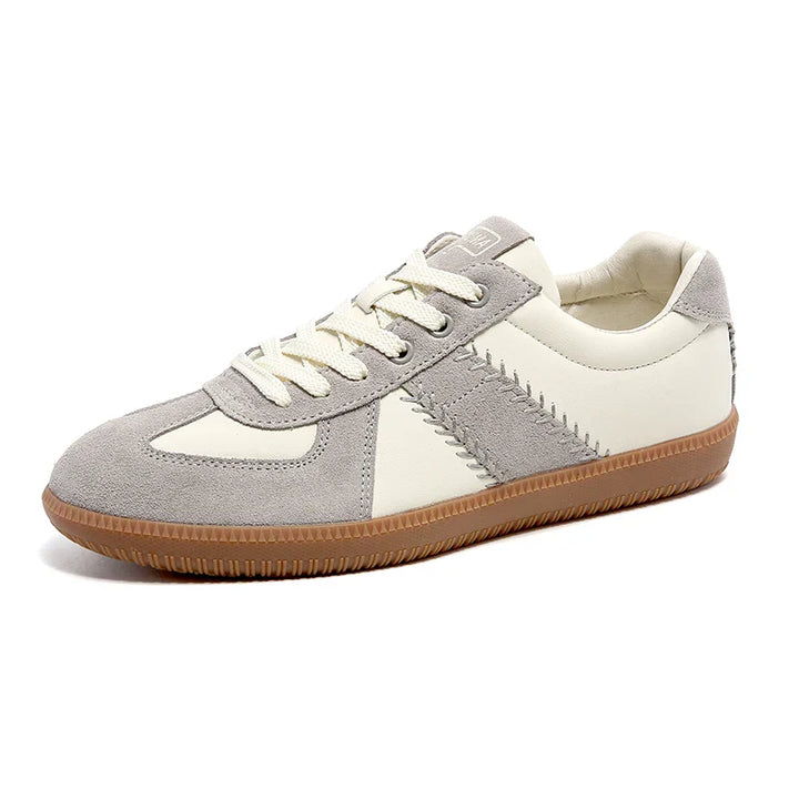 A stylish sneaker with a gray suede toe and trim, off-white leather panels, white laces, decorative stitching, and a textured brown rubber sole—these lightweight breathable sneakers offer comfort and modern appeal.