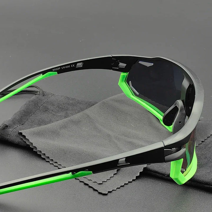 Close-up of Olympus Sunglasses with black frames and green accents, featuring polarized lenses, resting on a black cleaning cloth and pouch against a dark background.