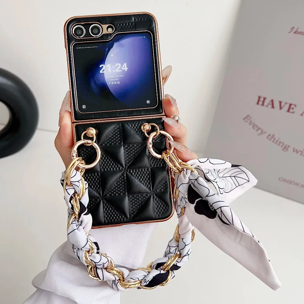 A hand holds a black, quilted Samsung Galaxy Z Flip premium leather case with gold chain and scarf details. The phone displays the time (21:24) and date. A blurred white sign with pink text is visible in the background.