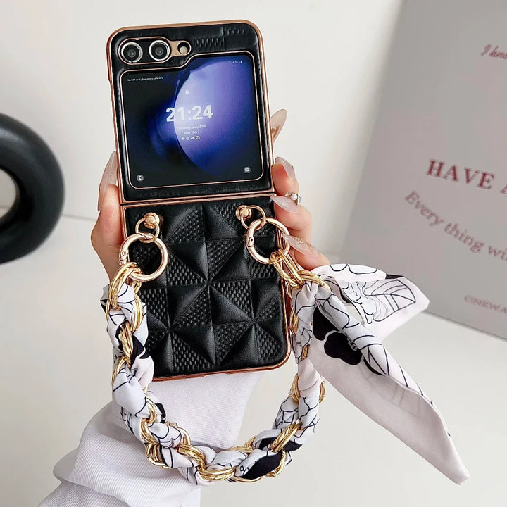 A hand holds a black, quilted Samsung Galaxy Z Flip premium leather case with gold chain and scarf details. The phone displays the time (21:24) and date. A blurred white sign with pink text is visible in the background.