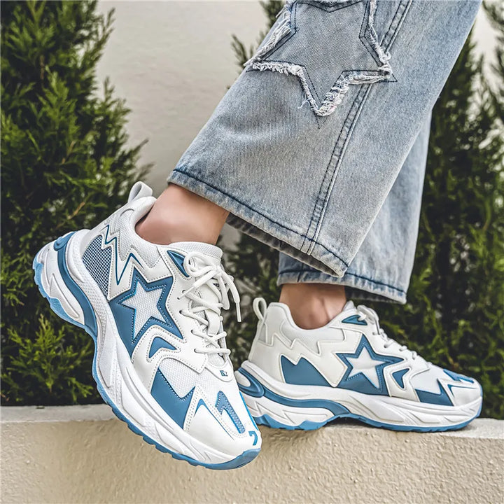 A person wearing light blue jeans with star patches and white sneakers featuring a durable rubber outsole stands on a ledge, with green bushes in the background.