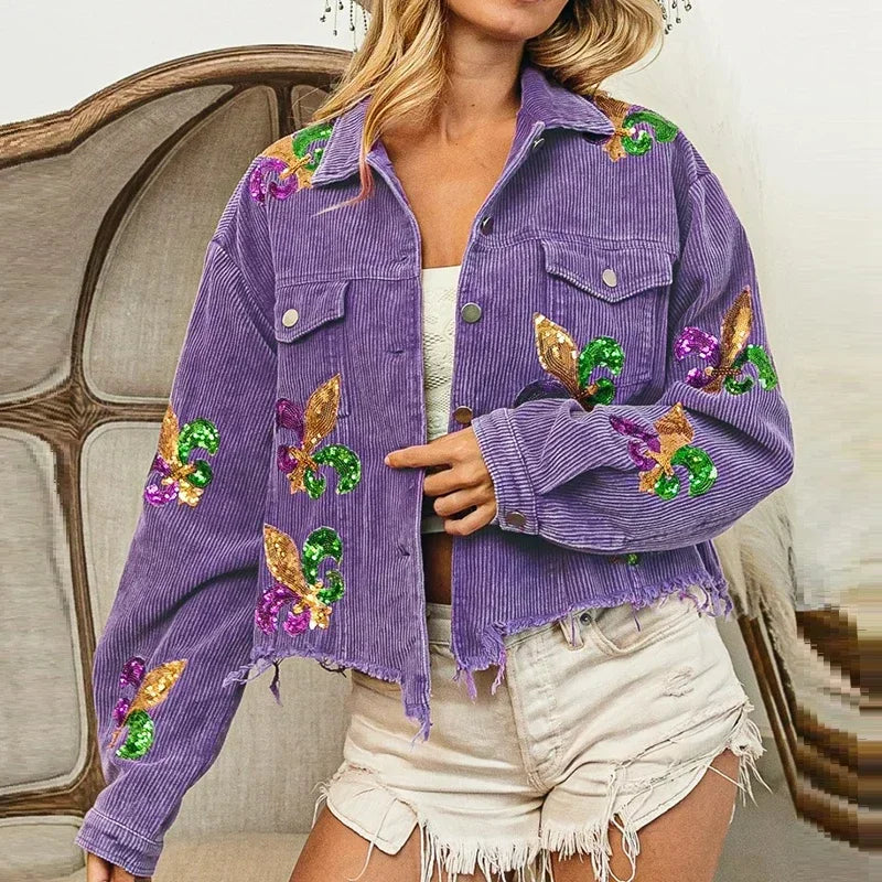 A woman wears a cropped relaxed fit purple corduroy jacket with colorful sequin floral patches and frayed edges, paired with a white top and light denim shorts.