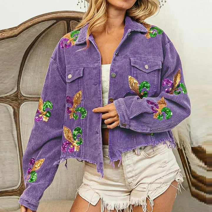 A woman wears a cropped relaxed fit purple corduroy jacket with colorful sequin floral patches and frayed edges, paired with a white top and light denim shorts.