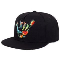 A black Hawaiian-inspired cap featuring an embroidered shaka hand sign adorned with vibrant tropical flowers and leaves in red, yellow, green, and blue on the front.