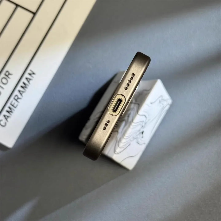 A close-up view of the bottom edge of a smartphone with a USB-C charging port and speaker grills, featuring a slim lightweight design and placed on a marble-patterned stand with a clapperboard partially visible in the background.