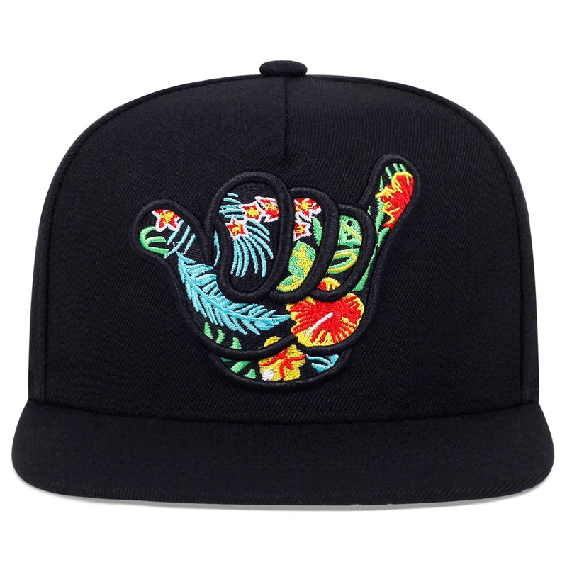 A black tropical snapback hat featuring an embroidered shaka hand symbol, filled with colorful floral patterns for a true Hawaiian-inspired cap vibe.