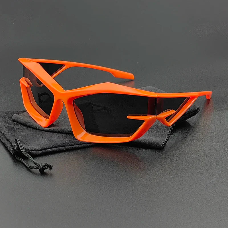Futuristic cycling glasses with bright orange geometric frames and high-contrast, UV400 protection lenses are displayed on a black drawstring pouch against a dark background.