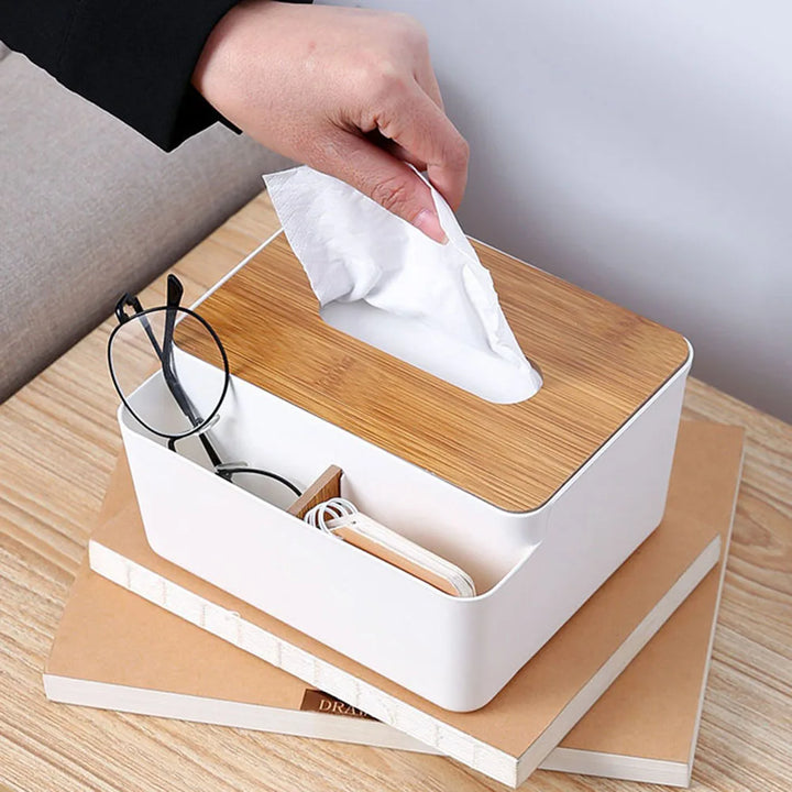 A hand pulls a tissue from a Table Wooden Cover Tissue Box, which also organizes glasses and earphones on its wooden lid. The stylish desktop organizer sits atop two stacked books, blending function with elegance.