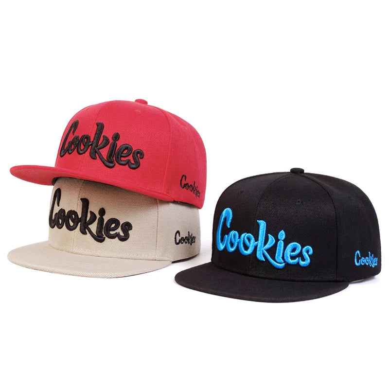Two snapback hats with Cookies embroidery on the front—one red with a beige brim and black text, the other black with blue text. Both feature embroidered side details and an adjustable strap for a perfect fit.