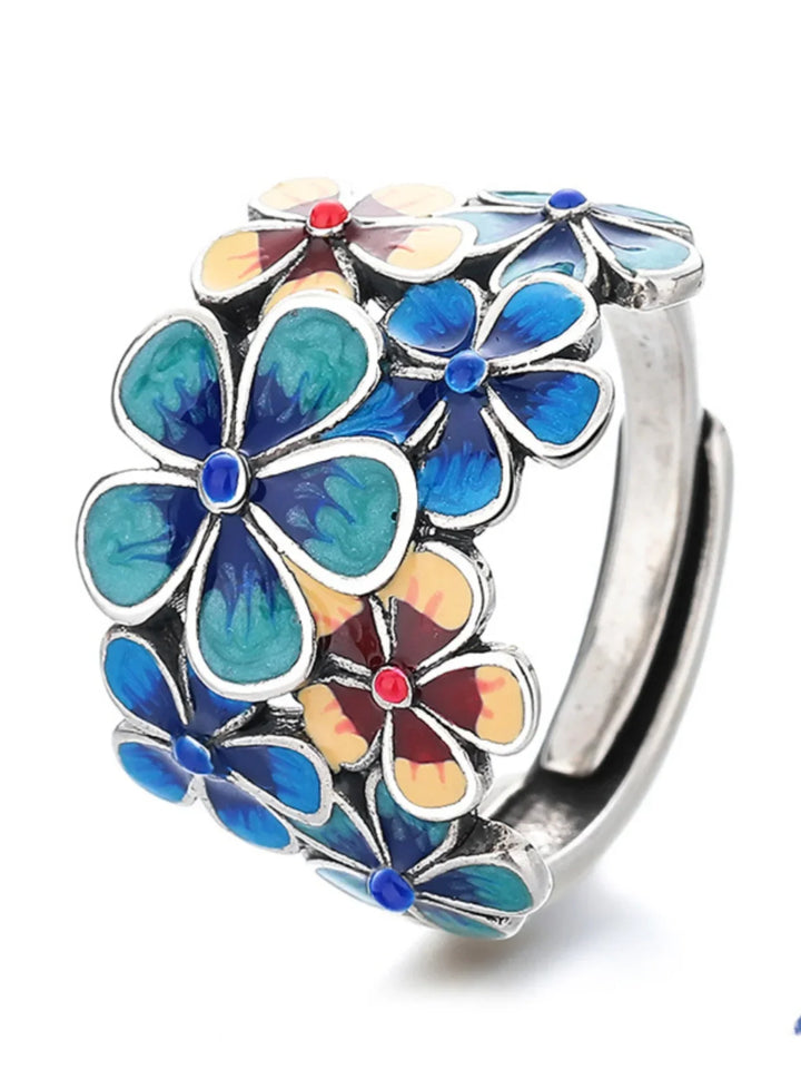 A silver ring decorated with vibrant colors of enamel flowers in blue, green, yellow, and red, featuring intricate petal designs and small colored centers reminiscent of stained glass.