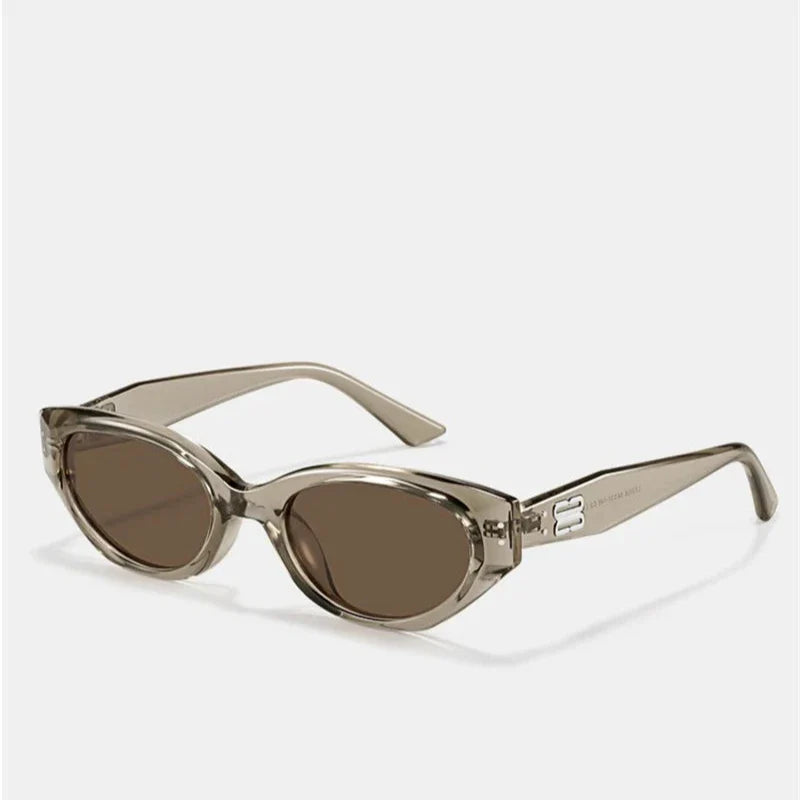 Transparent light brown oval sunglasses with a translucent acetate frame, dark brown scratch-resistant lenses, and thick, angled arms. Offers UV400 protection, displayed on a white background.