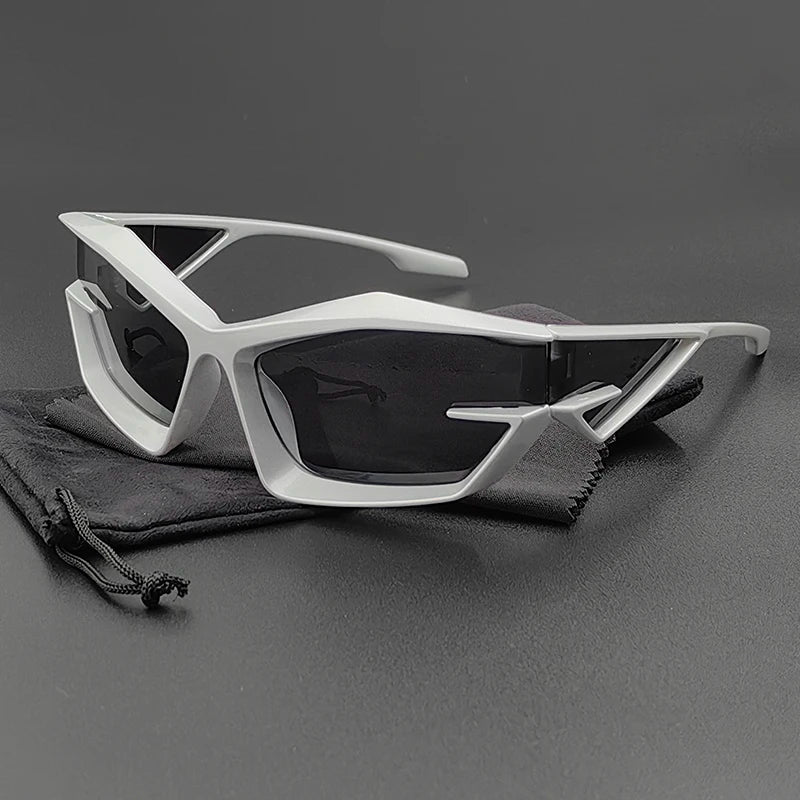 Futuristic, angular cycling glasses with silver geometric frames and high-contrast lenses, resting on a black drawstring pouch against a dark background.